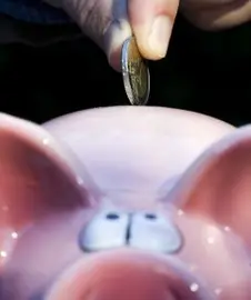 2008-10-09 HAARLEM - A hand puts a Euro coin in a pink piggy bank. ANP PHOTO XTRA KOEN SUYK